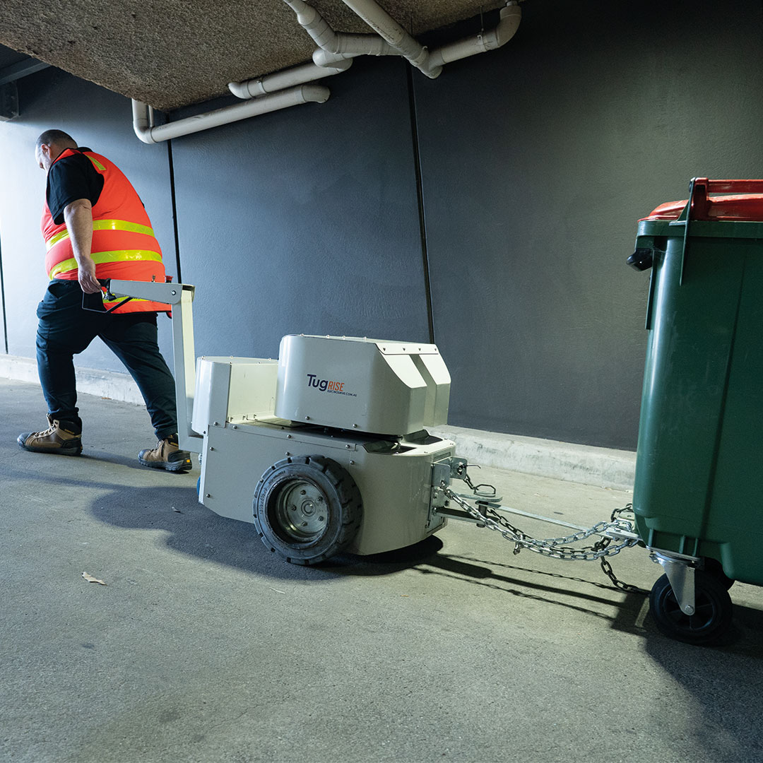 A powered tug towing a 1100 litre bin up a ramp